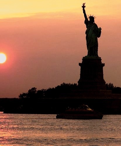 Statue of Liberty with water taxi at sunset, New York, USA